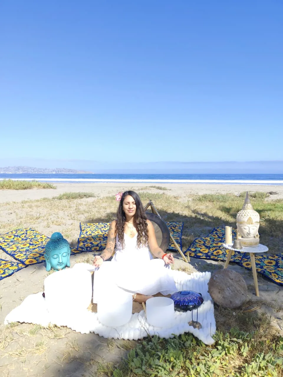 Bárbara meditando en la playa rodeada de cuencos de cuarzo y gong